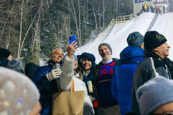 Group of people in winter outwear stand outdoors in snow among a crowd taking a picture at a nighttime event