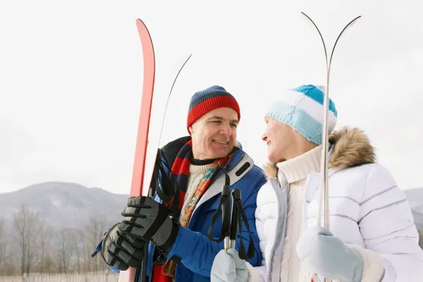 A man and woman  holding skis smile at eachother