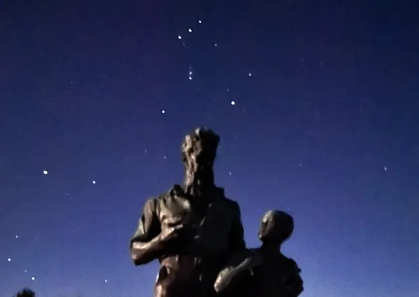 Blurry image of stars in the night sky behind an upshot angle of a John Brown and boy statue