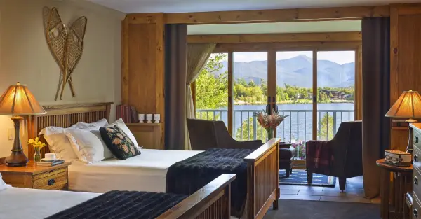 Beautifully appointed bedroom space with adirondack decor like snowshoes adorn the walls and the balcony windows open showing Mirror Lake and the majestic mountainscape background