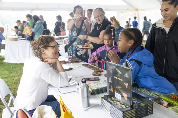 Young children and adults stand at book signing table talking to author