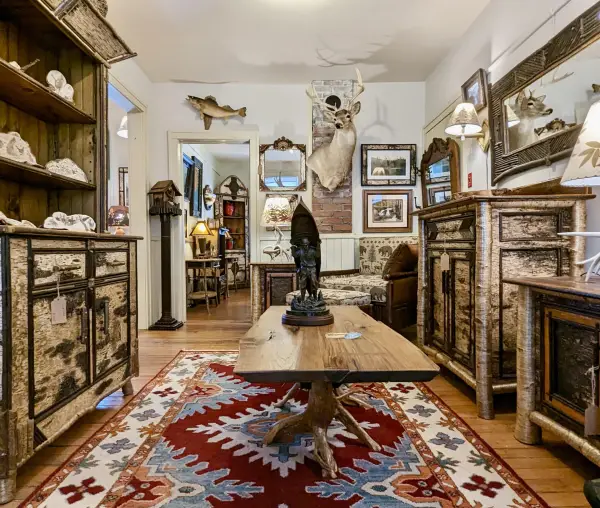 Large hutch and matching dresser made from white birch bark, a coffee table with live edge top and root ball base, a carving of a man carrying a canoe, mounts of various animals hang on the walls punctuated with mirrors surrounded with various barks.