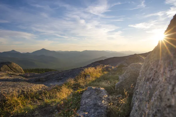View from mountain summit with sun peaking out from behind a large rock