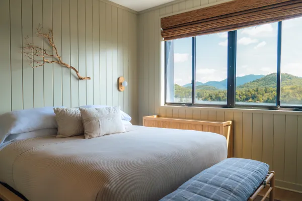 A mint green, minimal room at Laurel Lake Placid with light bedding and a view of Mirror Lake and surrounding mountains.