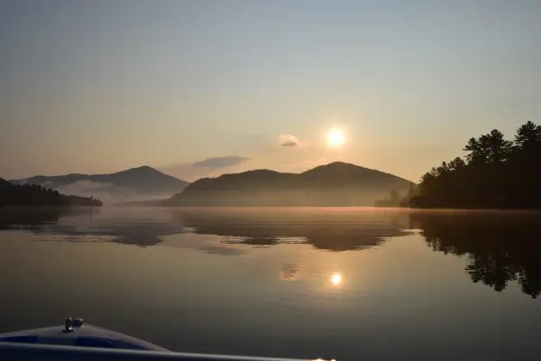 A ride on the boat on a smooth, misty lake with the mountains in the distance and the sun setting
