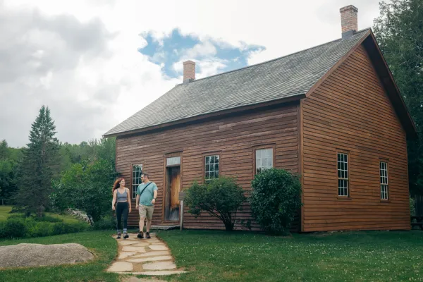 Couple in summer clothing walk out of barn at John Brown Farm State Historic Site in summer