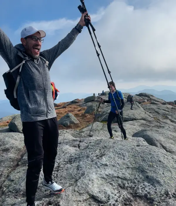 A very happy man raises his arm in sucess at the top of the summit