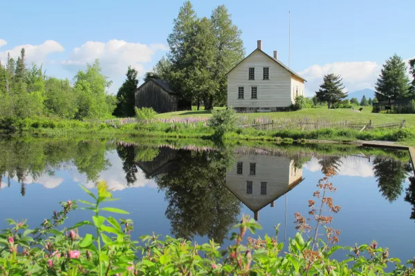 A 19th century farmhouse on a green lawn, reflected in a calm pond on a summer day.