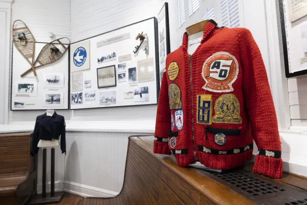 Sweater with patches on display at Lake Placid-North Elba Historical Society & Museum in front of displays on wall