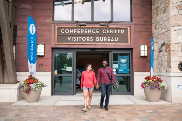 A man and woman walk out of a conference center in summer. 