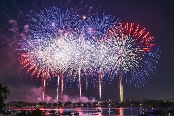 A vibrant fireworks display over a body of water, with the Washington Monument visible in the background.
