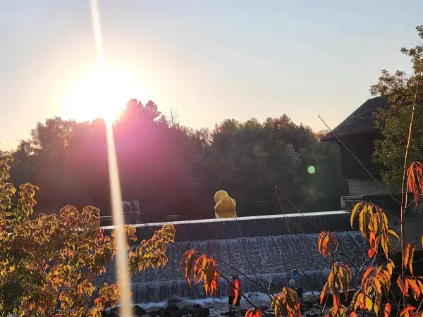 Large inflatable yellow duck floats in river above dam at sunset