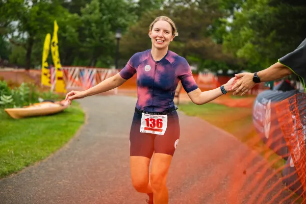 A smiling triathlete reaches out for a high-five while running toward the finish line of the Tupper Lake Tinman Triathlon.