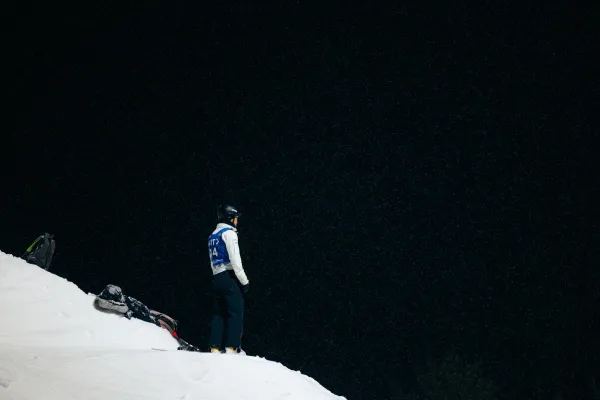 Freestyle aerial skier stands atop a snowy hill on a dark night looking out