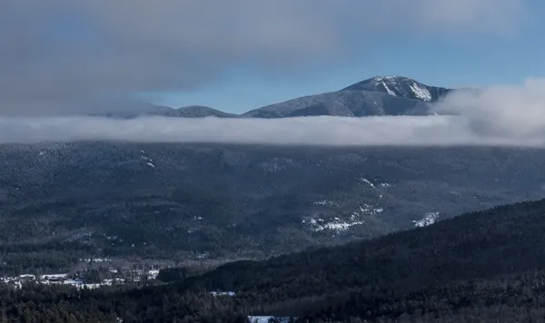 A tall mountain pokes through the clouds in the winter
