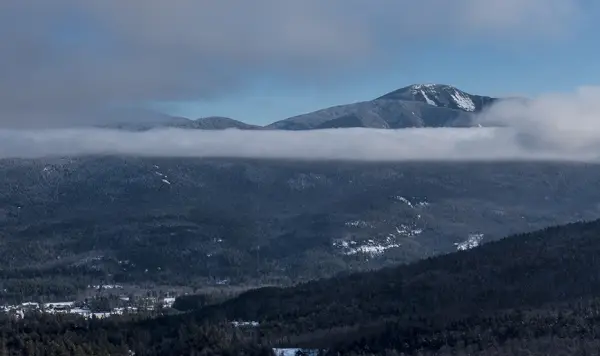 A tall mountain pokes through clouds in the winter