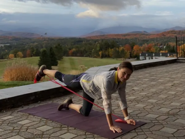 Woman doing a leg extension exercise with a resistance band outdoors with scenic mountain view in the background.