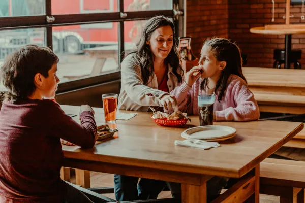 A mother and her kids enjoy a meal at big zs in front of the large glass garage doors.  Photo Credit to A. Kelly.