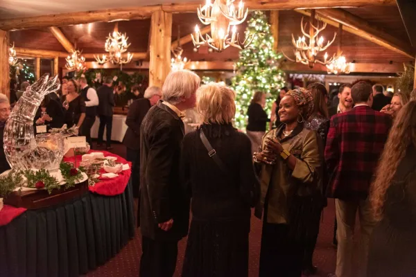 People mingle with drinks in hand amid buffet tables and Christmas trees and decor in an upscale lodge room