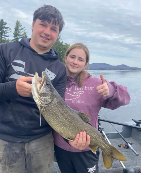 A man and woman hold a large fish and give a thumbs up.