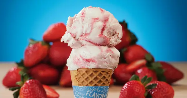 Double scoop of creamy strawberry ice cream in a waffle cone with blue background and ringed with red juicy strawberries