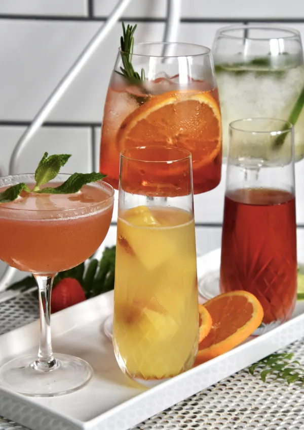 Tray of colorful cocktails in various glass types on a white plate with citrus garnishes