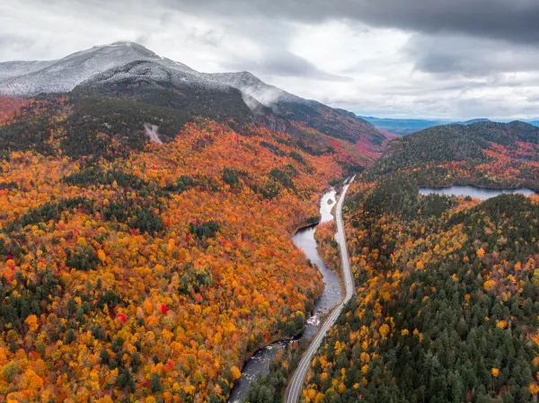 An aerial view of a snow-touched mountain and fall colored trees