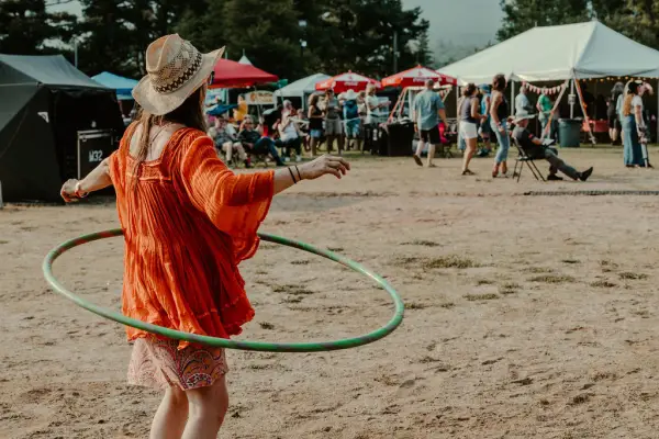 Woman in red dress and straw hat hula hoops in front of smallfestival crowd