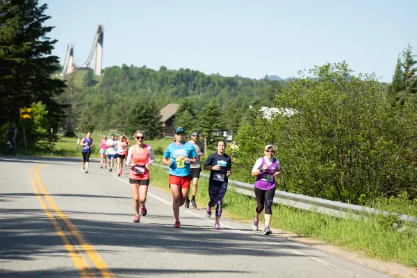 Runners run along a road with the ski jumps in the background