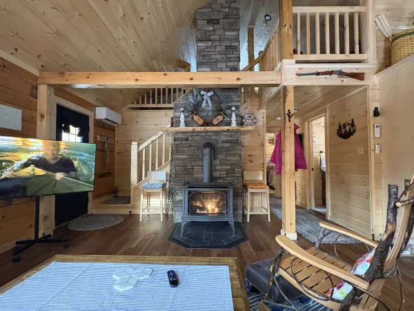 The living space with central stacked stone fireplace and wood stove with stairs to the loft behind.