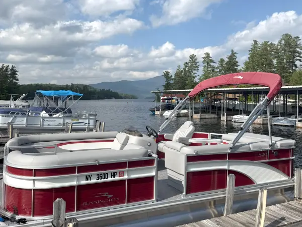 A red and white pontoon boat parked at the marina with a mountain surrounded with white billowing clouds