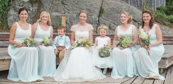 Bridal party, flower girl and ring bearer sit by a boulder.