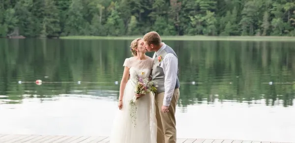 Bride and groom exchange a kiss by a lake.