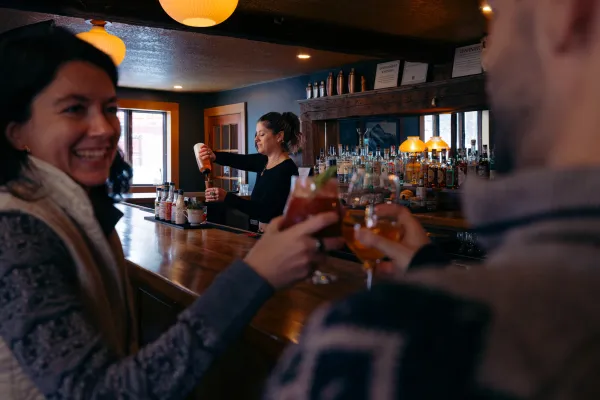 A man and woman cheers beers at a cozy bar.