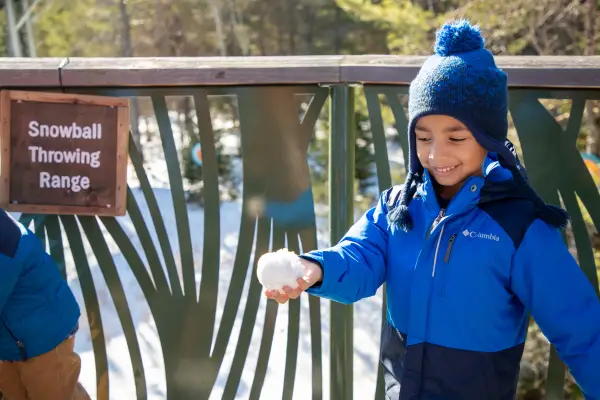 A young child gleefully looks down at his hand holding a freshly made snowball