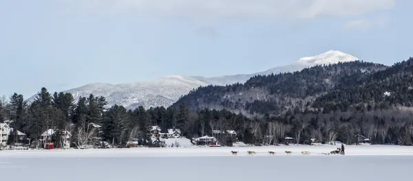A dog sled team races across a frozen lake with mountains in the background.