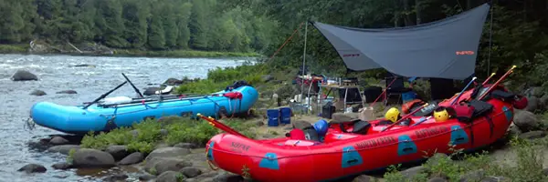 Inflatable rafts on the edge of the river with tents in the background