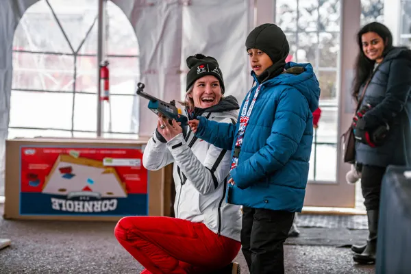A female biathlete shows her rifle to a child at a biathlon event.