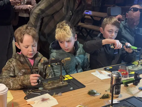 Three kids tying fly fishing flies at table