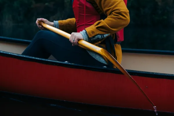 Shoulder down shot of person sitting in red canoe wearing red pfd holding wooden paddle