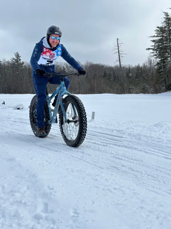 Cyclist in a helmet rides a fat-tire bike on a snowy trail, surrounded by a winter forest.