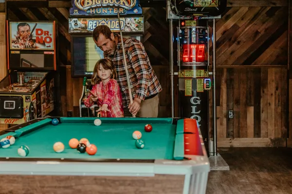 A father and daughter play billiards with an assortment of arcade style games behind.  Photo Credit to A. Kelly.