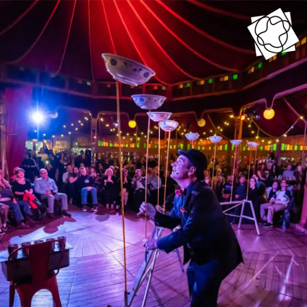 Circus performer spins plates on the wooden poles on stage in front of audience