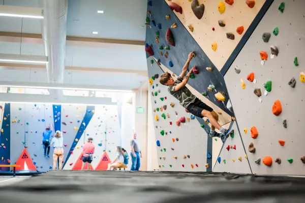 A teenage boy climbs a cantilvered indoor rock climbing wall.
