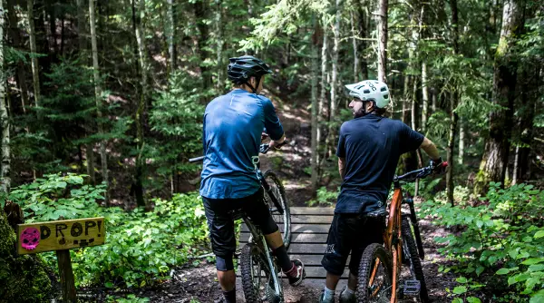 A pair of mountain bikers take a break before crossing a mountain biking bridge.