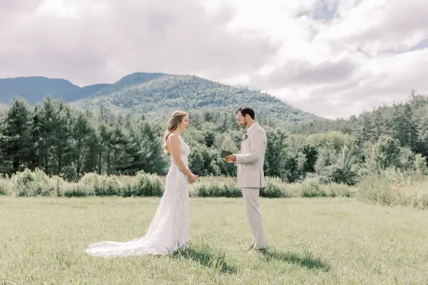 Bride and groom face each other in a grassy field with mountain views
