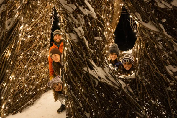 children peaking around art with christmas lights 