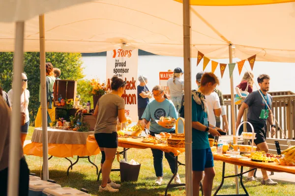 Under a tent, volunteers and participants gather around tables with fruit and snacks at the Adirondack Marathon.