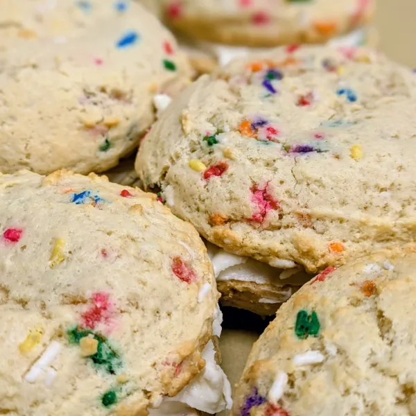 Cookie sandwiches made with rainbow sprinkle cookies and filled with whipped cream.
