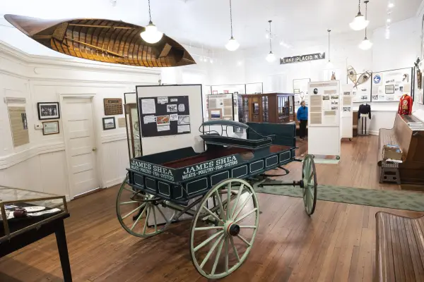Interior of Lake Placid-North Elba Historical Society & Museum with old carriage in center of room, wooden canoe hung on wall, and displays on white walls
